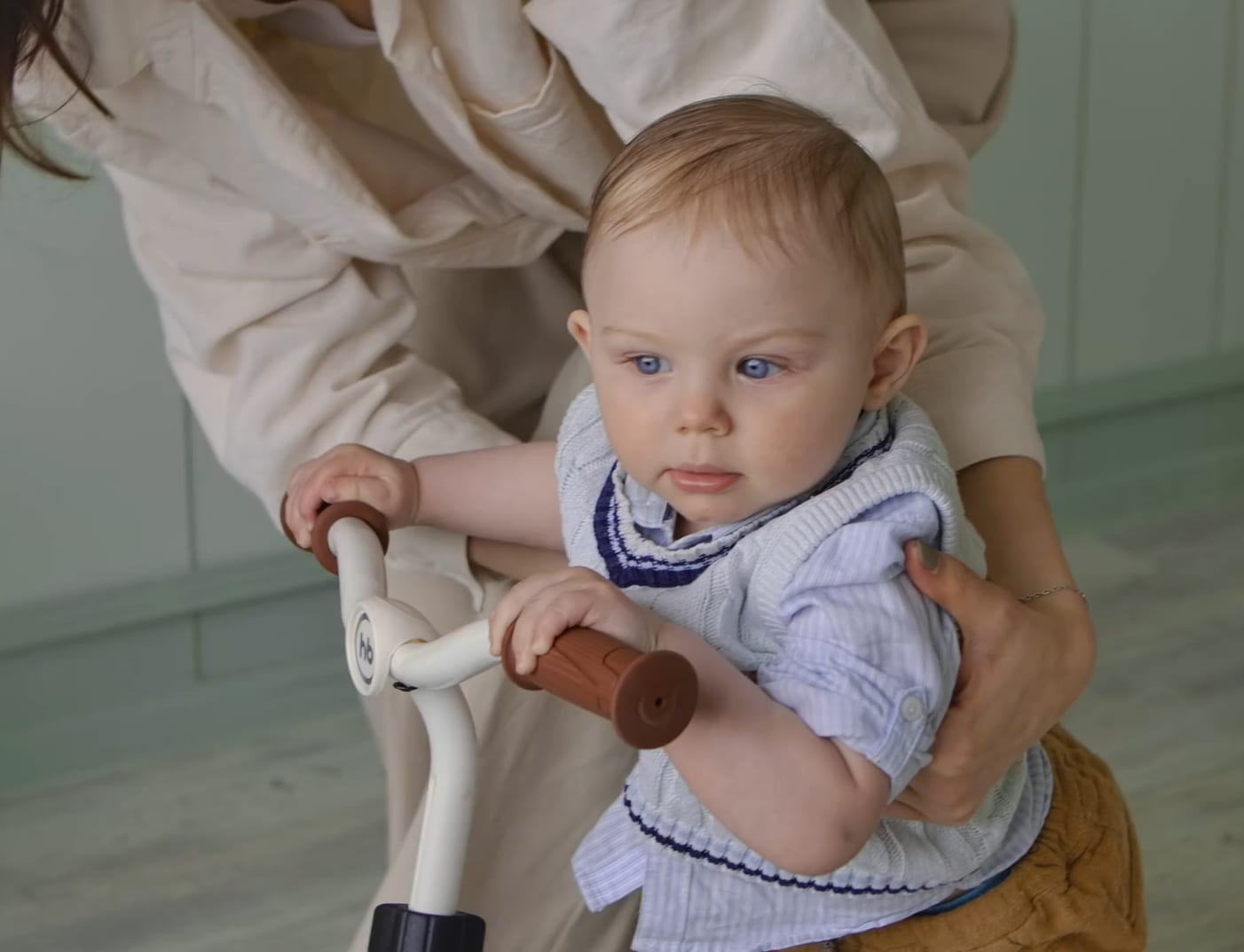 Baby on a wooden tricycle steadied by his mother